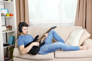 Young man with guitar on sofa in room