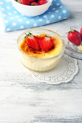 Creme brulee dessert with fresh strawberry berries on napkin, on color wooden background