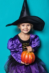 Portrait of little girl in black hat and witch clothing with pumpkin. Halloween