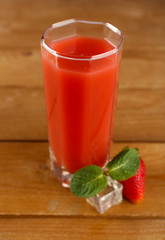 Glass of fresh strawberry juice on wooden background