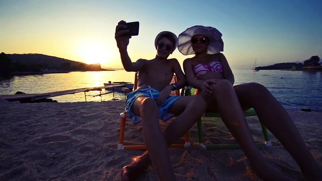 taking selfie pictures by beautiful models boy and girl with Smartphone at buach Sunset. Models lit with reflector light, VINTAGE