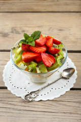 Dessert of fresh fruits in glass saucer on wooden table, closeup