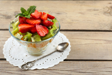 Dessert of fresh fruits in glass saucer on wooden table, closeup