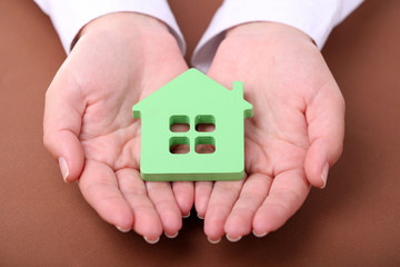 Female hands holding house on color background