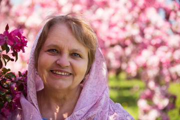 Fototapeta premium Happy adult woman in kerchief under purple flowers in garden