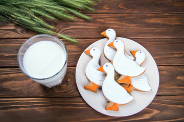 Tasty gingerbread suck shaped cookies on a plate with glass of milk and with ear of wheat on a wooden background