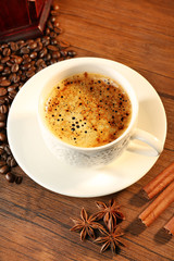 Cup of fresh spicy coffee with beans on table, closeup