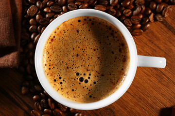 Cup of fresh coffee with beans on table, closeup