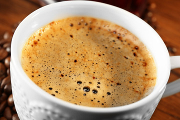 Cup of fresh coffee with beans on table, closeup