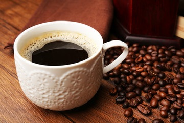 Cup of fresh coffee with beans on table, closeup
