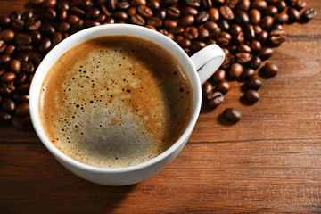 Cup of fresh coffee with beans on table, closeup