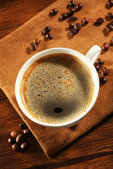 Cup of fresh coffee with beans on table, closeup