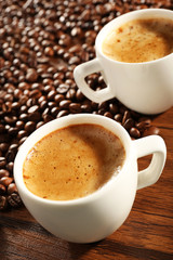 Two cups of fresh coffee with beans on table, closeup