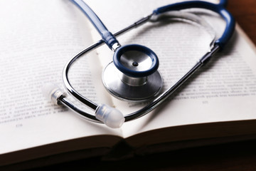 Stethoscope on book on wooden table, closeup