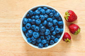 Blueberries in the ceramic bowl with strawberries aside on the wood