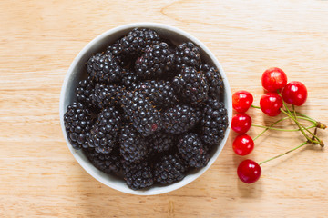 Blackberries in the ceramic bowl with cherries aside on the wood