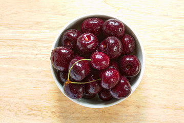 Red sweet cherries with water drops in the ceramic bowl on the wood