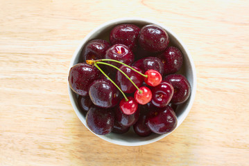 Red sweet cherries with water drops in the ceramic bowl on the wood