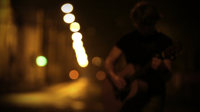 A young male guitarist perfoming on the night empty street