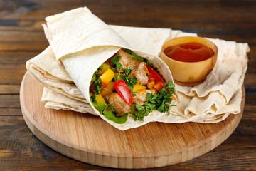 Homemade tasty burrito with vegetables on cutting board, on wooden background
