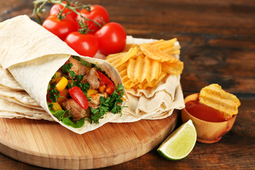 Fototapeta na wymiar Homemade tasty burrito with vegetables and potato chips on cutting board, on wooden background