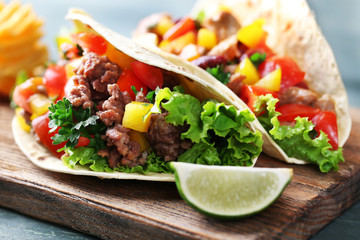 Homemade beef burritos with vegetables and tortilla, on cutting board, on wooden background