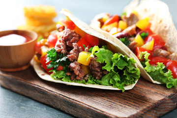 Homemade beef burritos with vegetables and tortilla, on cutting board, on wooden background