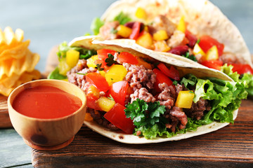 Homemade beef burritos with vegetables, potato chips on cutting board, on wooden background