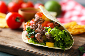 Homemade beef burrito with vegetables, potato chips on cutting board, on wooden background
