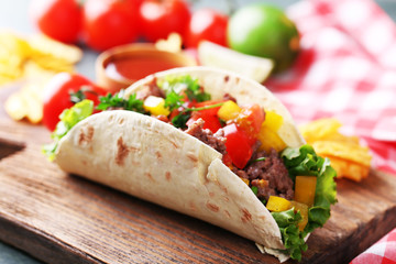 Homemade beef burrito with vegetables, potato chips on cutting board, on wooden background