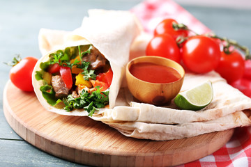 Homemade tasty burrito with vegetables, potato chips on cutting board, on wooden background