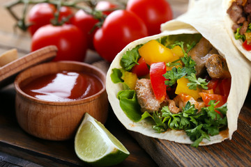 Homemade tasty burrito with vegetables on cutting board, on wooden background