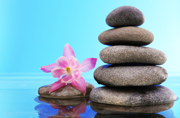 Naklejka na ściany i meble Stack of spa stones with flower on blue background