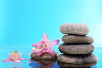 Obraz na płótnie Canvas Stack of spa stones with flowers on blue background
