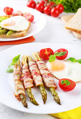 Dish of asparagus with bacon and egg in plate on table, closeup