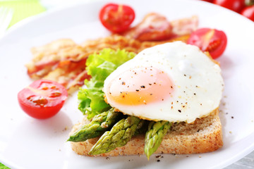 Dish of asparagus with bacon and egg in plate on table, closeup