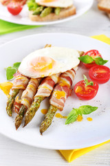 Dish of asparagus with bacon and egg in plate on table, closeup