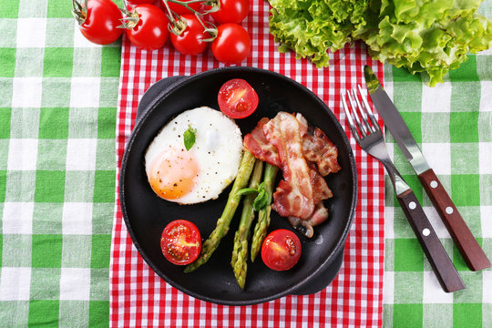 Dish of asparagus with eggs and bacon in pan on table, top view