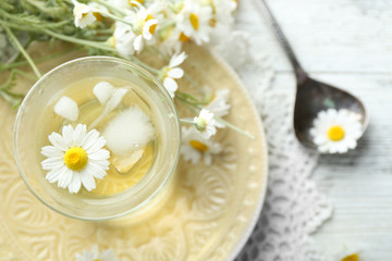 Glass of cold chamomile tea with ice cubes and chamomile flowers on color wooden background