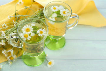 Glasses of chamomile tea with chamomile flowers on color wooden background