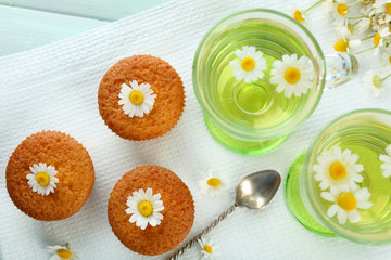 Glass of chamomile tea with chamomile flowers and tasty muffins on color wooden background