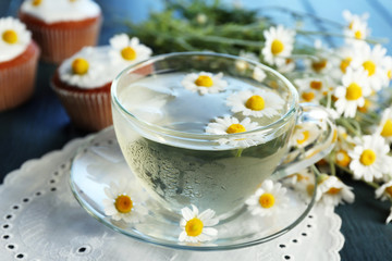 Cup of chamomile tea with chamomile flowers and tasty muffins on color wooden background