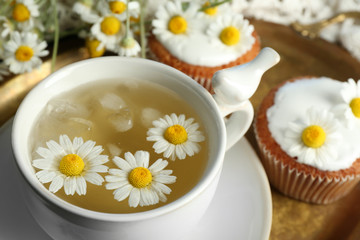 Fototapeta na wymiar Cup of chamomile tea with chamomile flowers and tasty muffins on tray, on color wooden background
