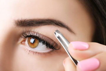 Naklejka premium Young woman plucking eyebrows with tweezers close up