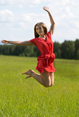 Young girl in a red dress jumping in a field coniferous forest