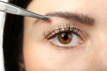 Naklejka premium Young woman plucking eyebrows with tweezers close up