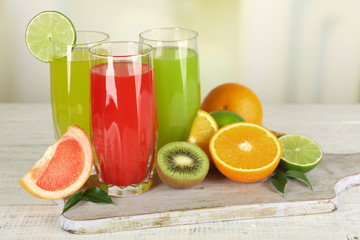 Glasses of different juice with fruits and mint on bright background