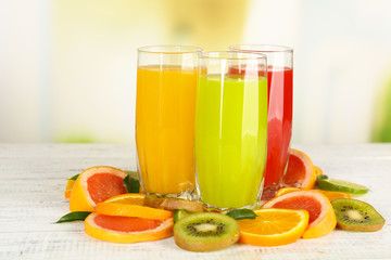 Glasses of different juice with fruits and mint on bright background