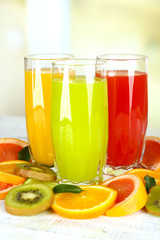 Glasses of different juice with fruits and mint on bright background