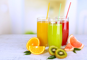 Glasses of different juice with fruits and mint on bright background